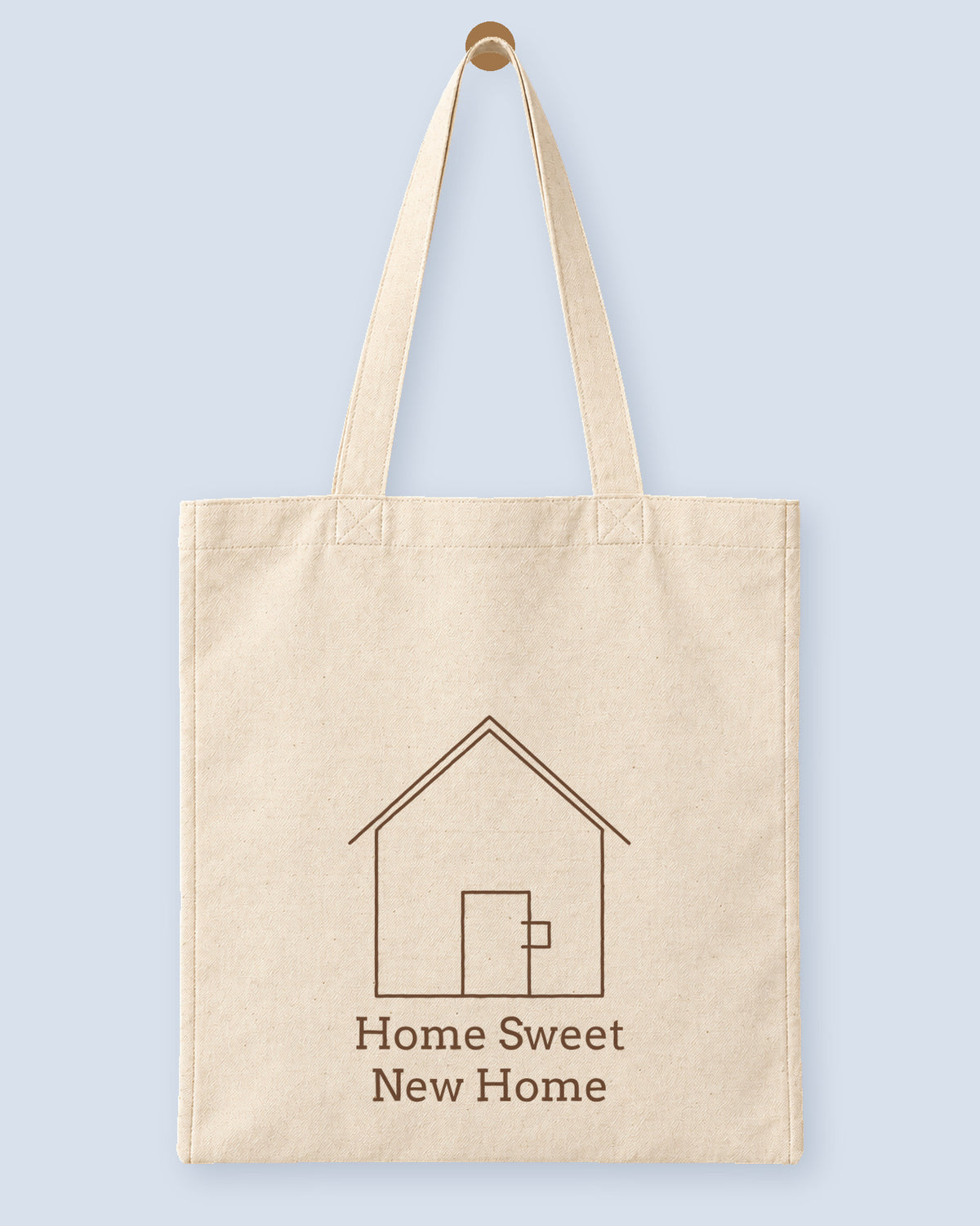 Natural canvas tote printed with “Home Sweet New Home”, hanging on a wooden peg.
