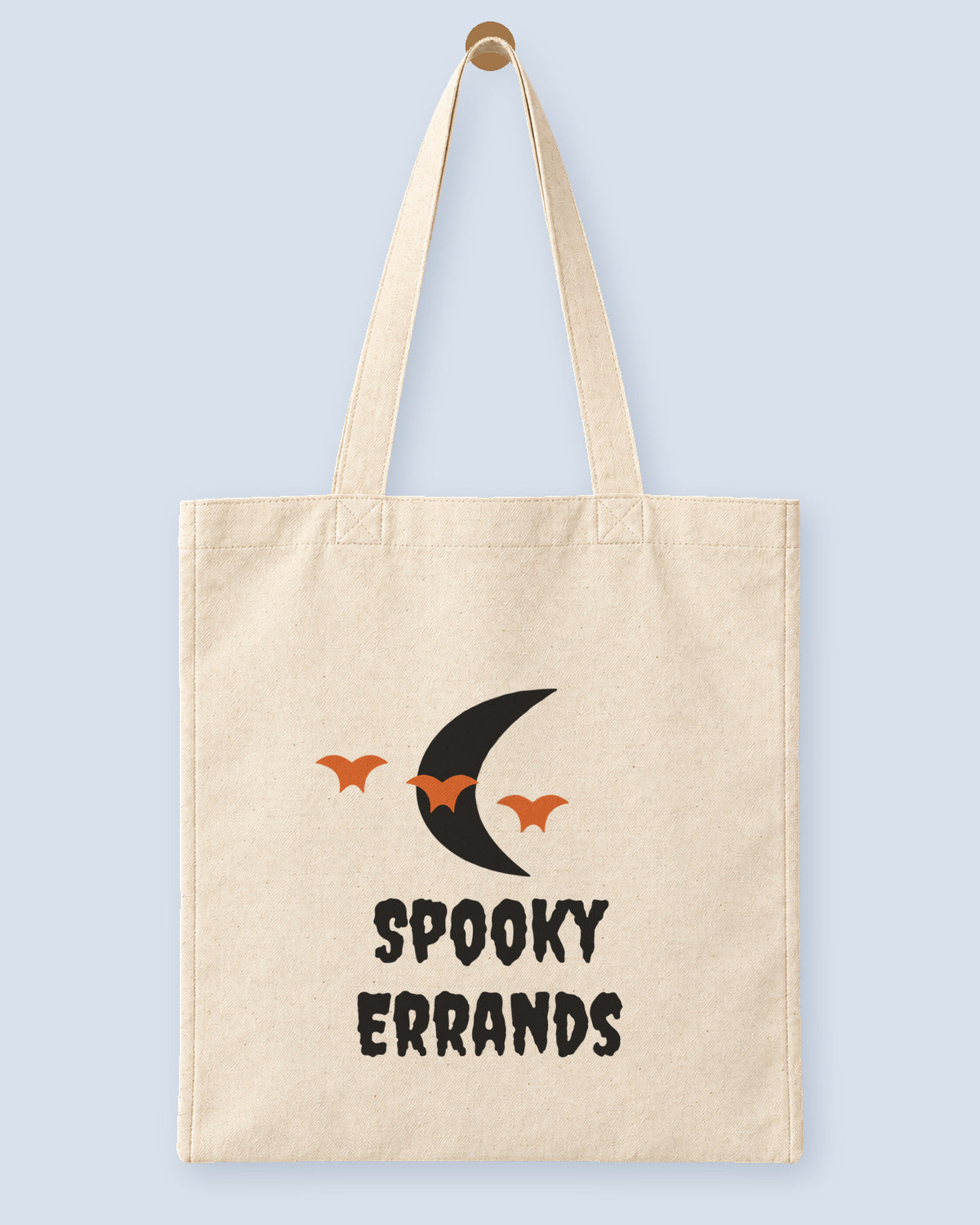 Natural canvas tote printed with “Spooky Errands”, hanging on a wooden peg.