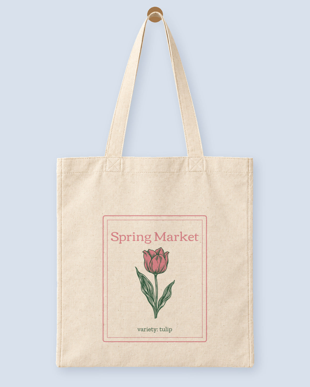 Natural canvas tote printed with “Spring Market”, hanging on a wooden peg.