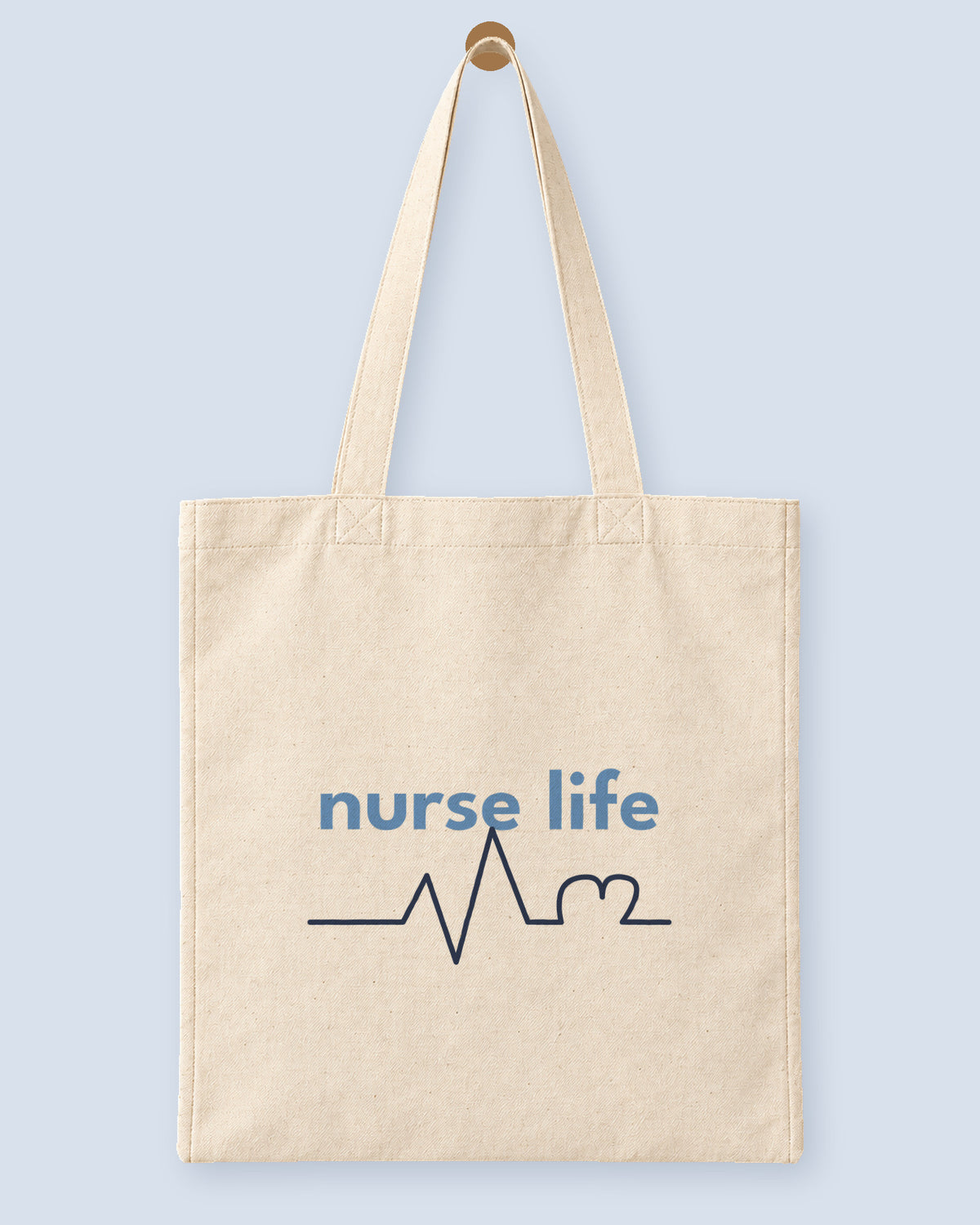 Natural canvas tote printed with “nurse life”, hanging on a wooden peg.