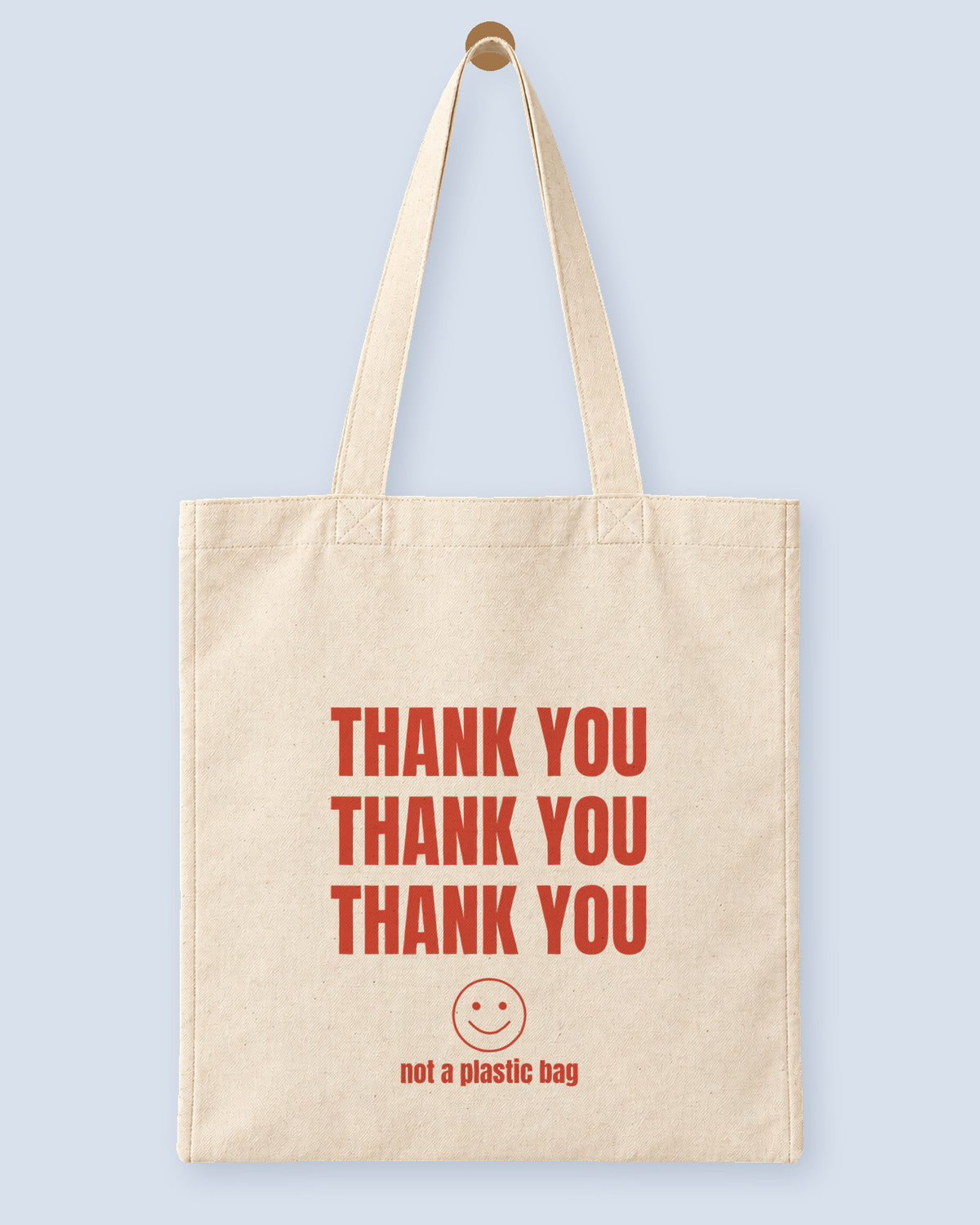 Natural canvas tote printed with “THANK YOU”, hanging on a wooden peg.