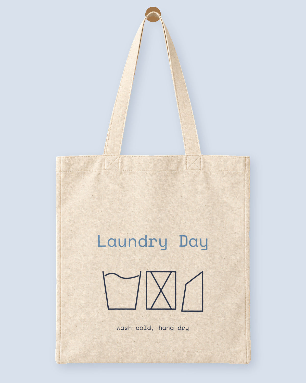 Natural canvas tote printed with “Laundry Day”, hanging on a wooden peg.