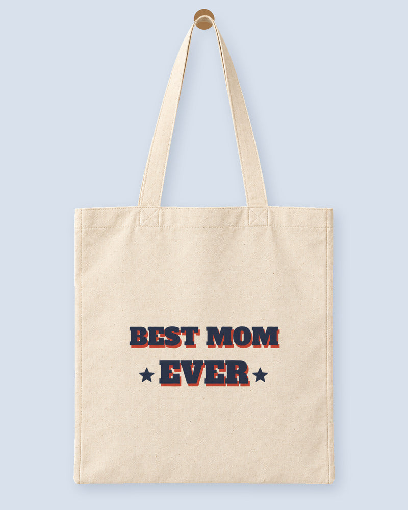 Natural canvas tote printed with “BEST MOM EVER”, hanging on a wooden peg.