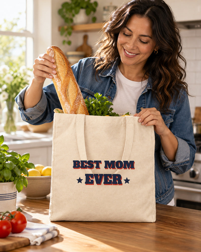 Latina woman carrying a natural canvas tote printed with “BEST MOM EVER” in navy, red. Styled digital image.