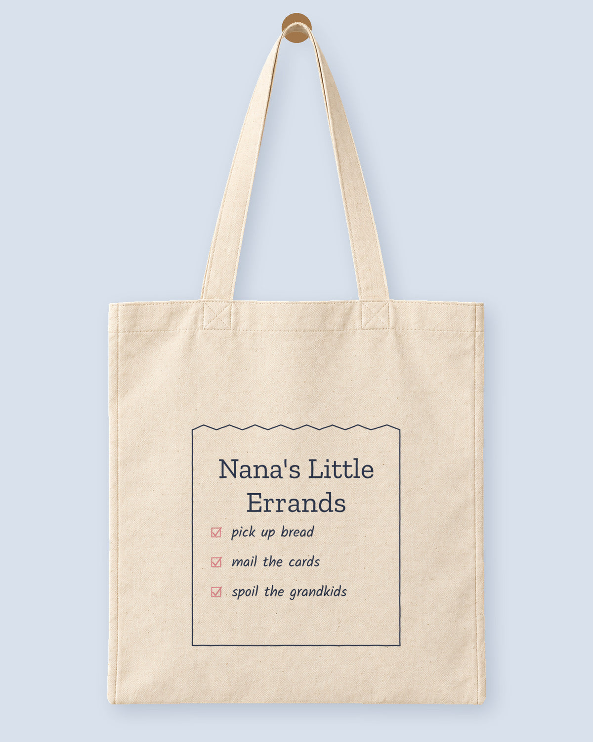 Natural canvas tote printed with “Nana's Little Errands”, hanging on a wooden peg.