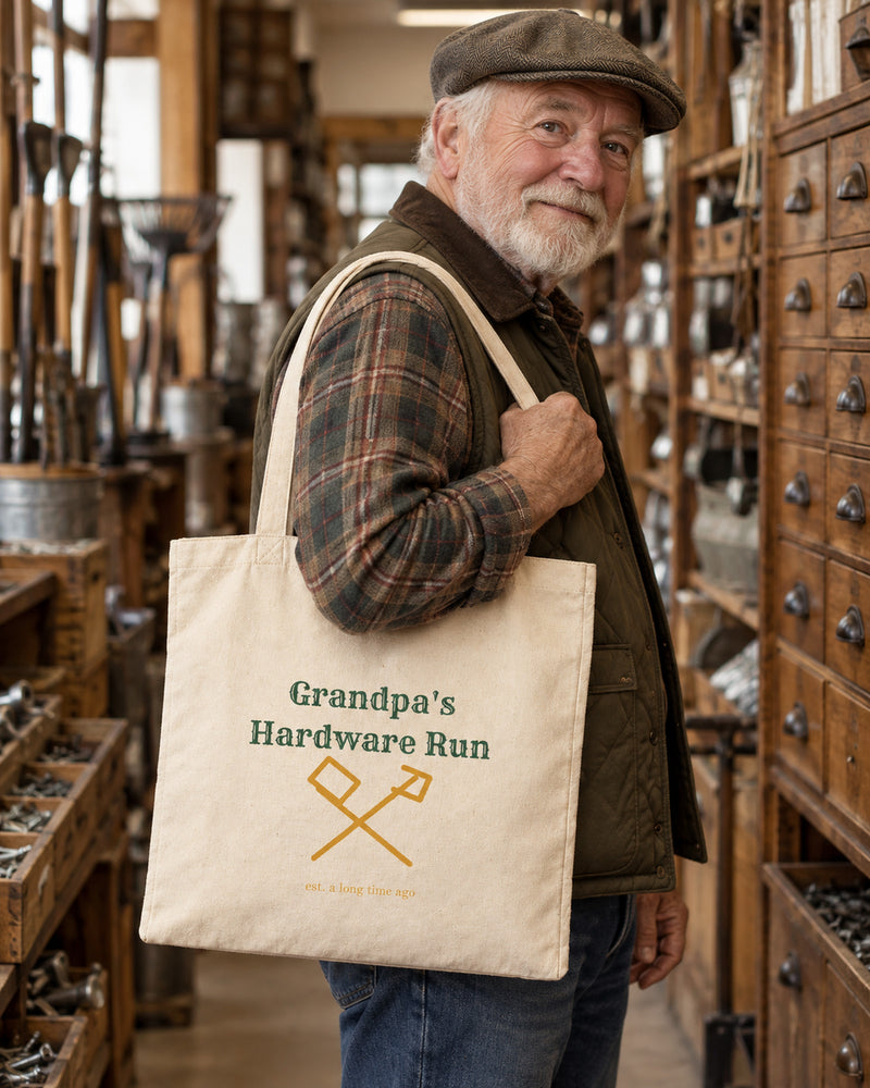 White man carrying a natural canvas tote printed with “Grandpa's Hardware Run” in forest, marigold. Styled digital image.