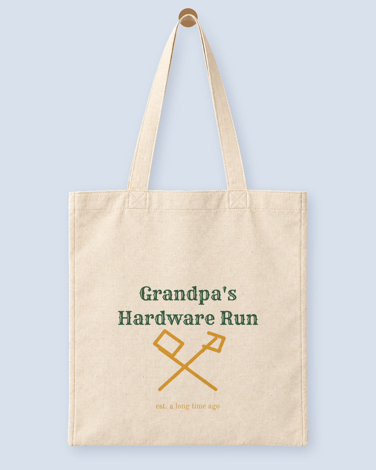 Natural canvas tote printed with “Grandpa's Hardware Run”, hanging on a wooden peg.