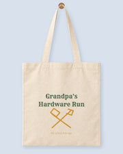 Natural canvas tote printed with “Grandpa's Hardware Run”, hanging on a wooden peg.