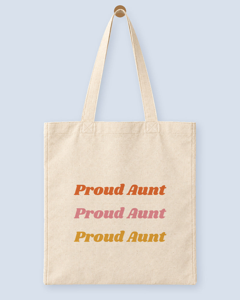 Natural canvas tote printed with “Proud Aunt”, hanging on a wooden peg.