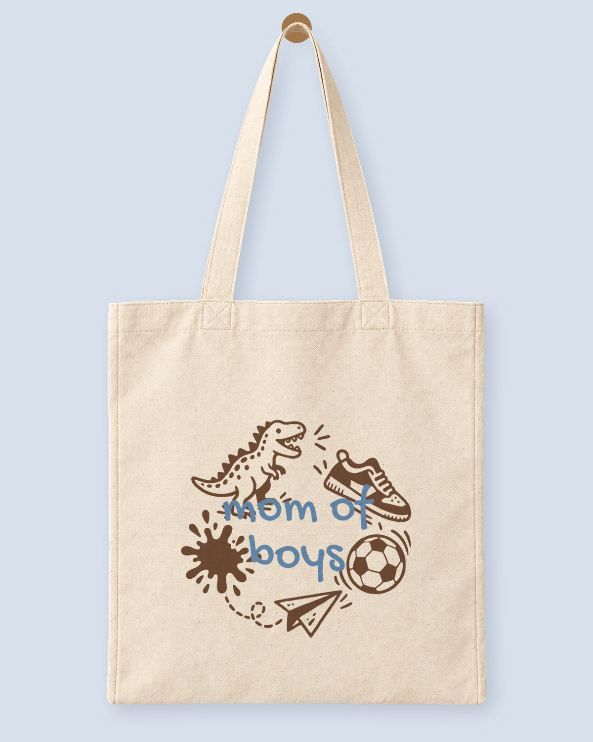 Natural canvas tote printed with “mom of boys”, hanging on a wooden peg.