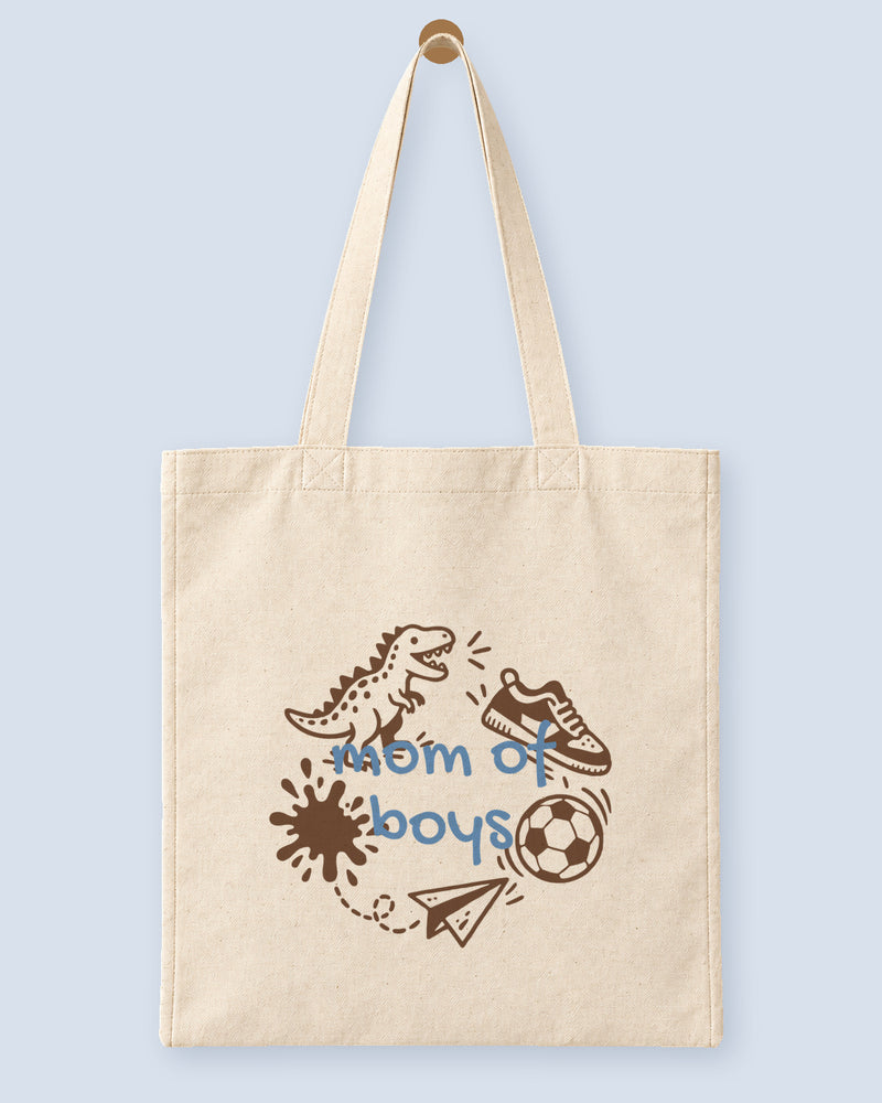 Natural canvas tote printed with “mom of boys”, hanging on a wooden peg.