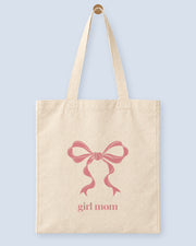 Natural canvas tote printed with “girl mom”, hanging on a wooden peg.