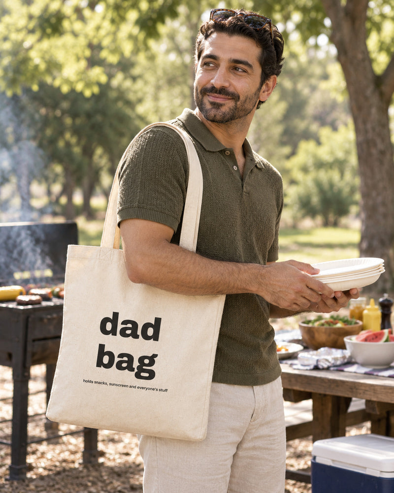 Middle eastern man carrying a natural canvas tote printed with “dad bag” in black. Styled digital image.