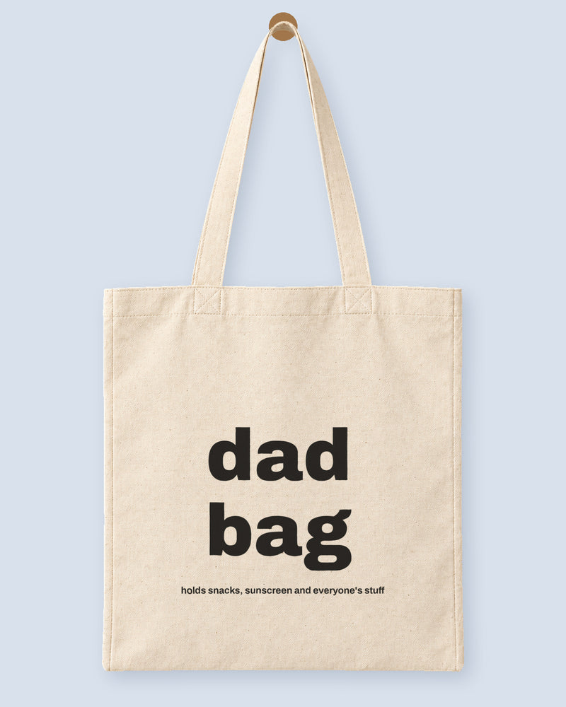 Natural canvas tote printed with “dad bag”, hanging on a wooden peg.