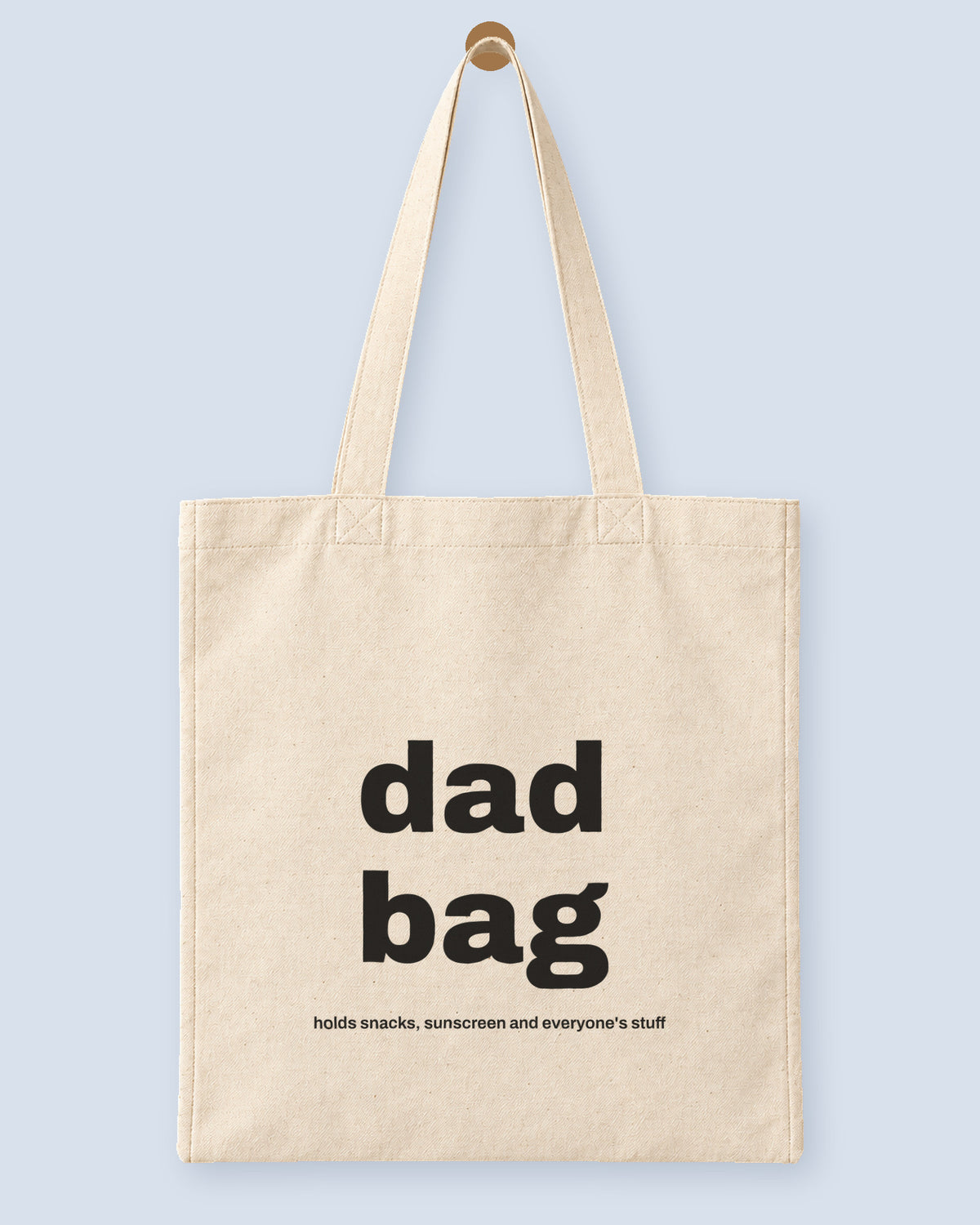 Natural canvas tote printed with “dad bag”, hanging on a wooden peg.