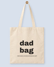 Natural canvas tote printed with “dad bag”, hanging on a wooden peg.