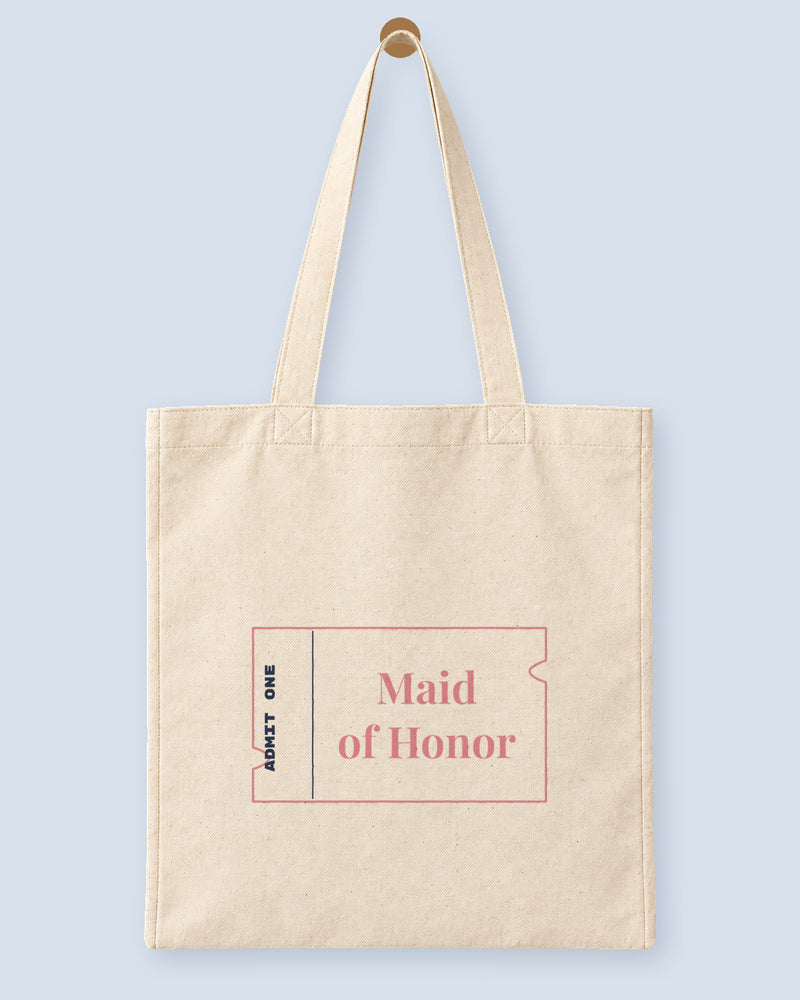 Natural canvas tote printed with “Maid of Honor”, hanging on a wooden peg.