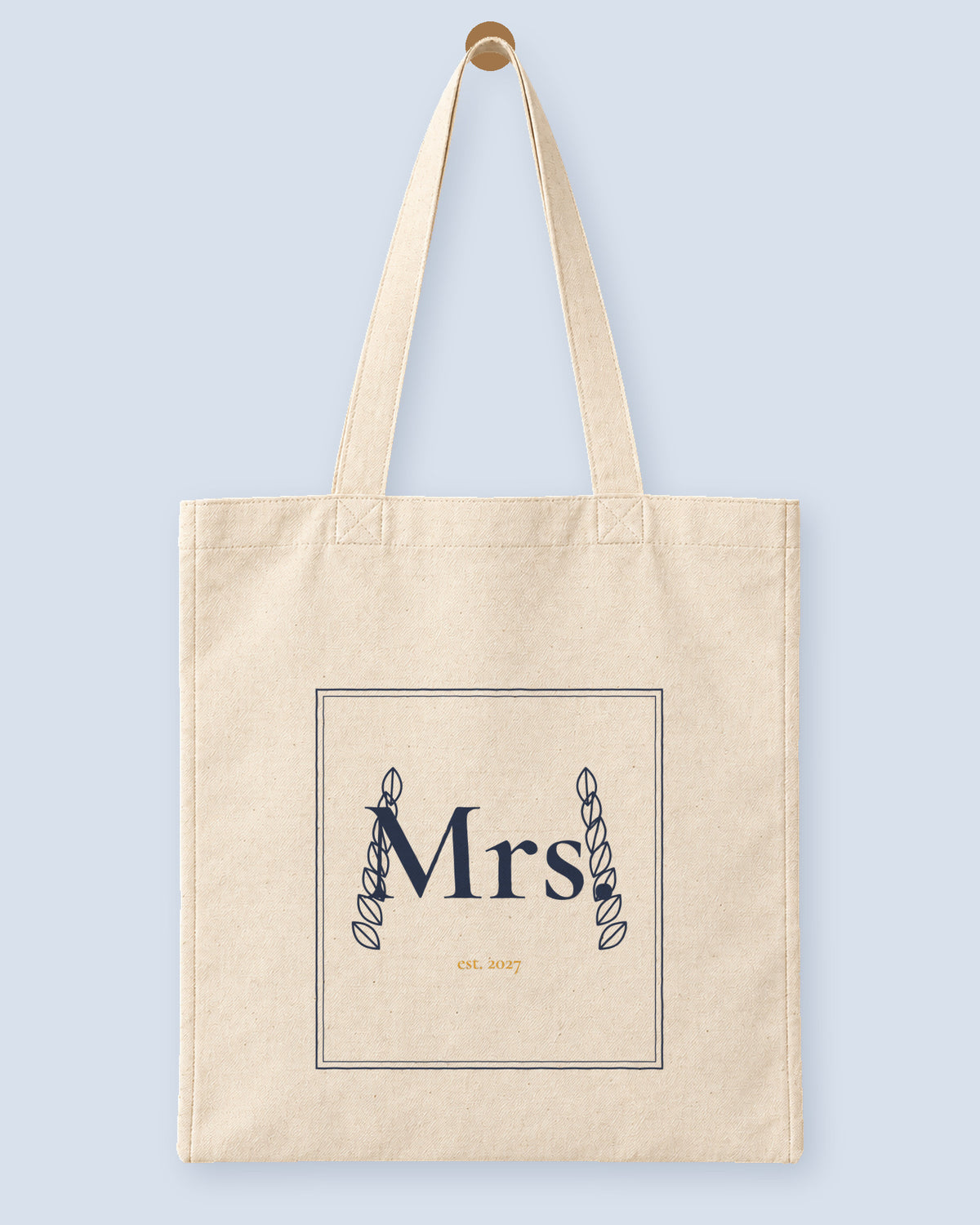 Natural canvas tote printed with “Mrs.”, hanging on a wooden peg.