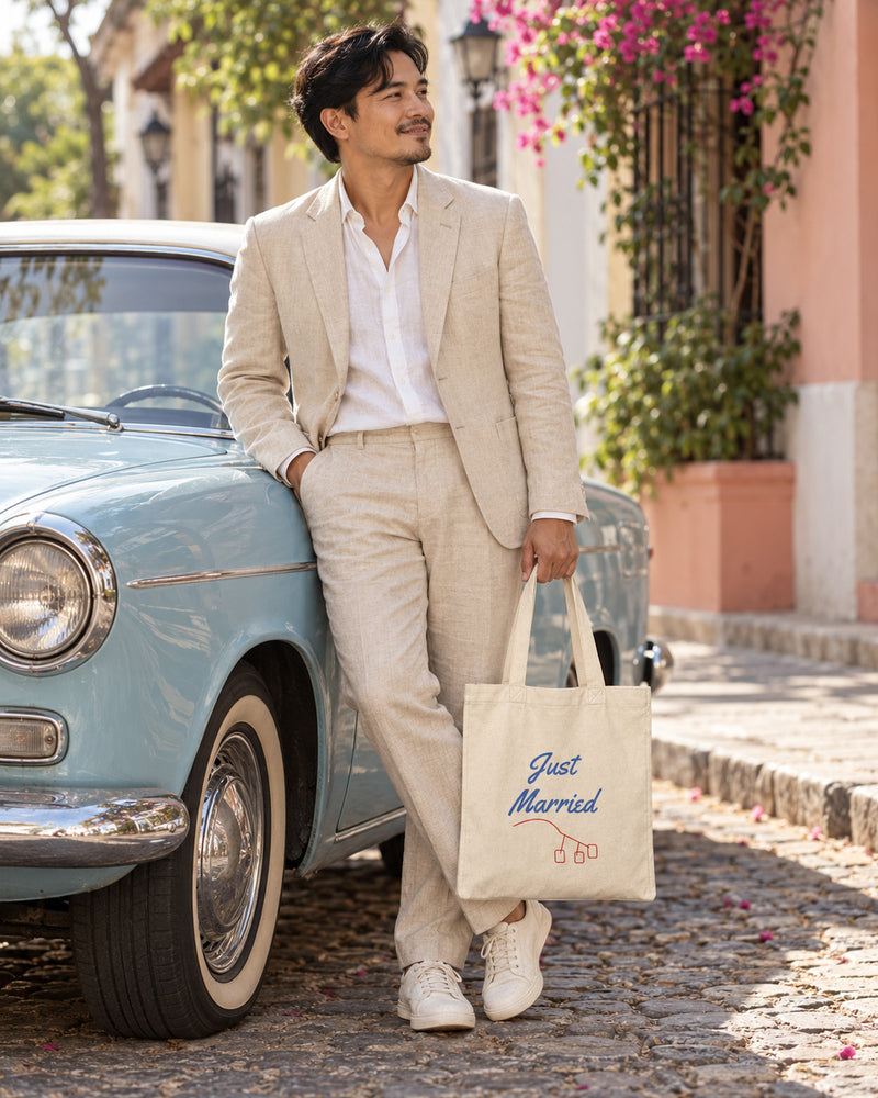 Filipino man carrying a natural canvas tote printed with “Just Married” in sky, red. Styled digital image.