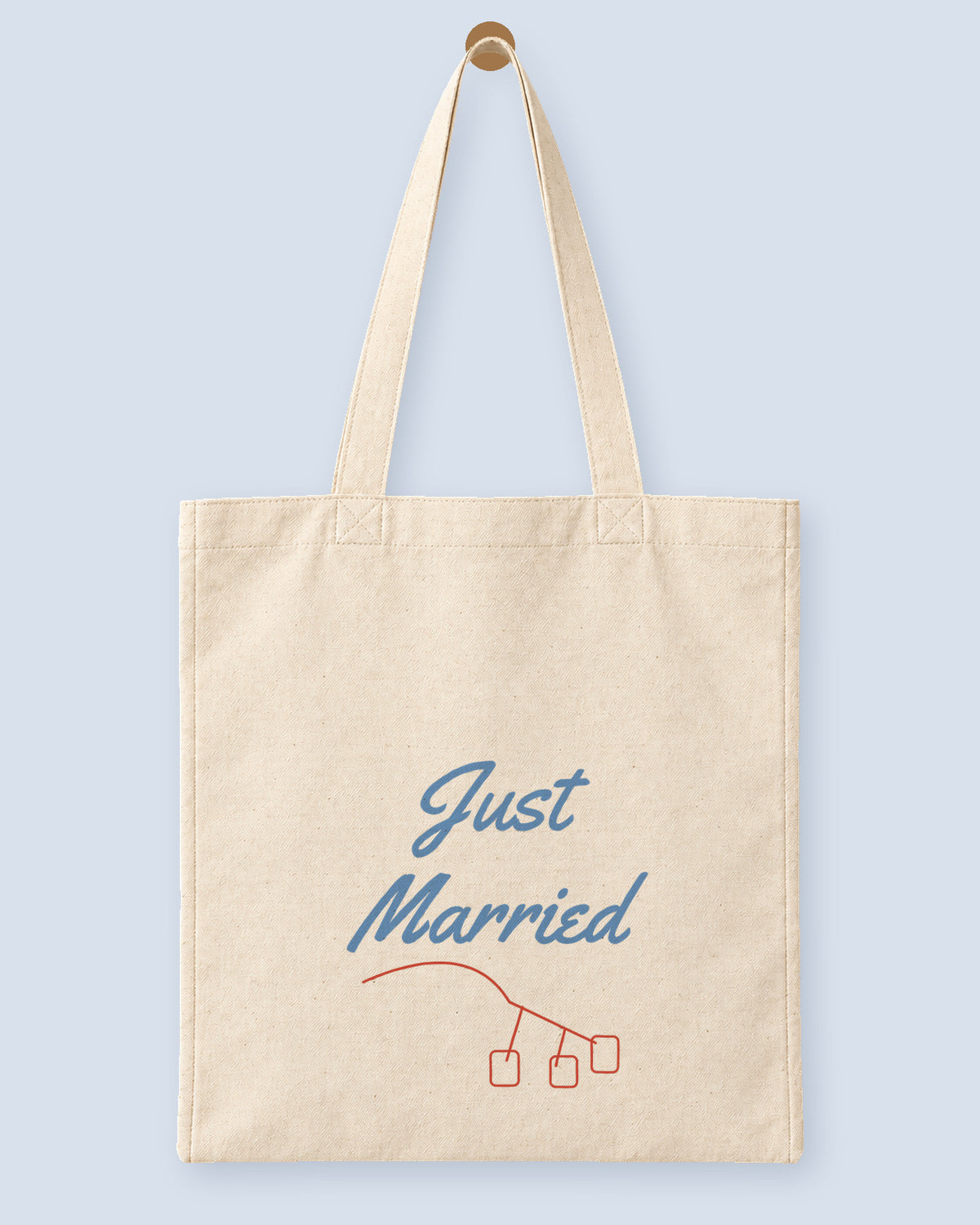 Natural canvas tote printed with “Just Married”, hanging on a wooden peg.