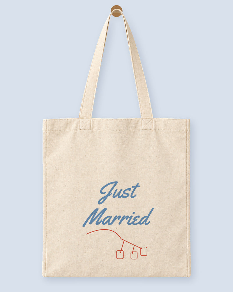 Natural canvas tote printed with “Just Married”, hanging on a wooden peg.
