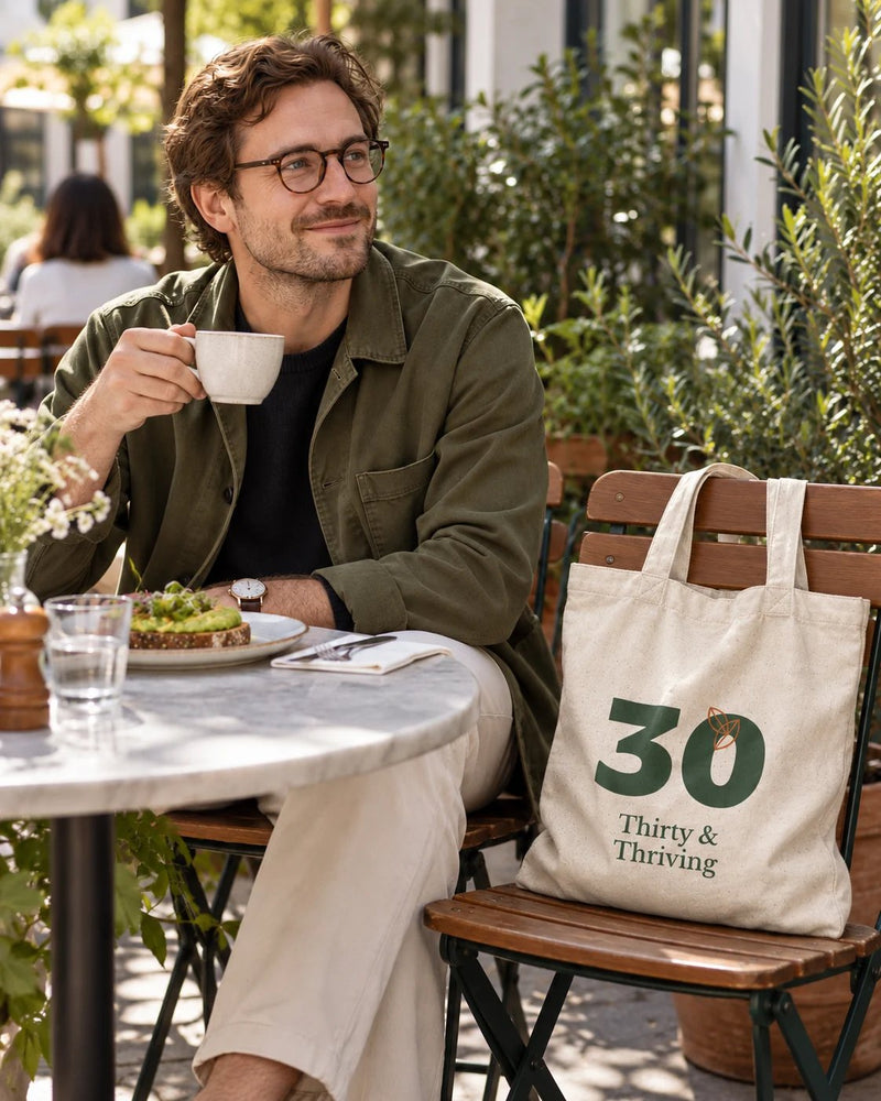 White man carrying a natural canvas tote printed with “Thirty & Thriving” in forest, orange. Styled digital image.