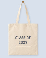 Natural canvas tote printed with “CLASS OF 2027”, hanging on a wooden peg.