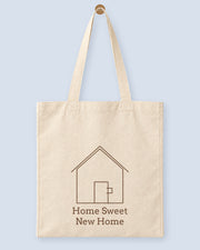 Natural canvas tote printed with “Home Sweet New Home”, hanging on a wooden peg.
