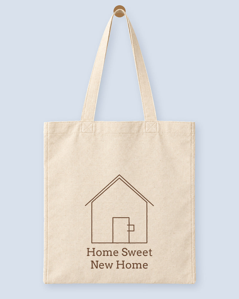 Natural canvas tote printed with “Home Sweet New Home”, hanging on a wooden peg.