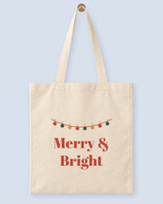 Natural canvas tote printed with “Merry & Bright”, hanging on a wooden peg.