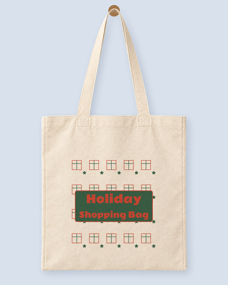 Natural canvas tote printed with “Holiday Shopping Bag”, hanging on a wooden peg.
