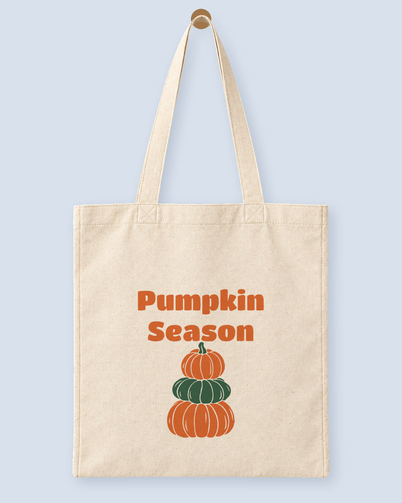 Natural canvas tote printed with “Pumpkin Season”, hanging on a wooden peg.