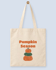 Natural canvas tote printed with “Pumpkin Season”, hanging on a wooden peg.