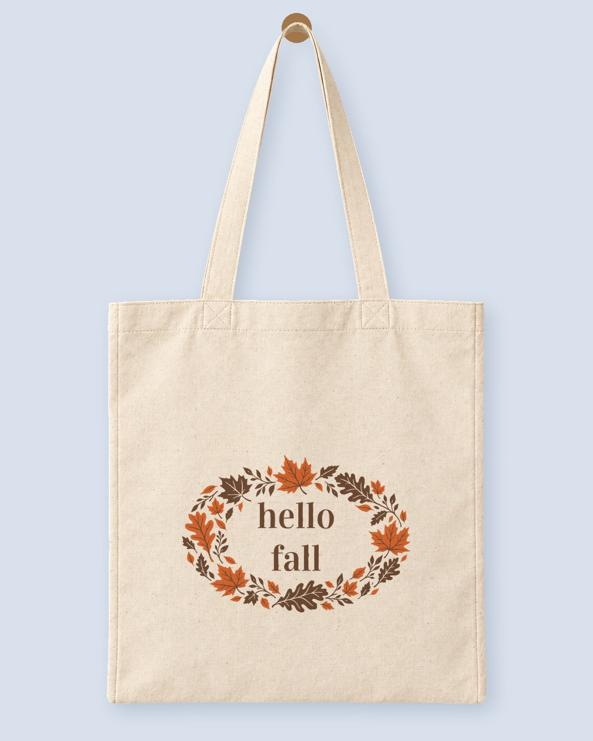 Natural canvas tote printed with “hello fall”, hanging on a wooden peg.