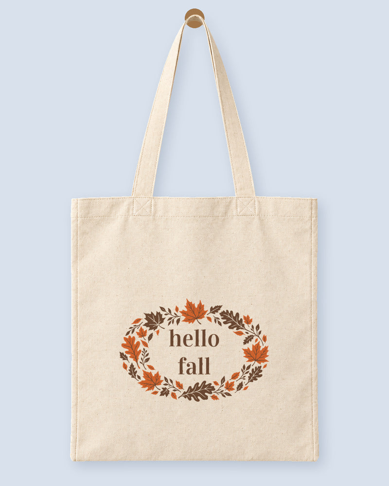 Natural canvas tote printed with “hello fall”, hanging on a wooden peg.