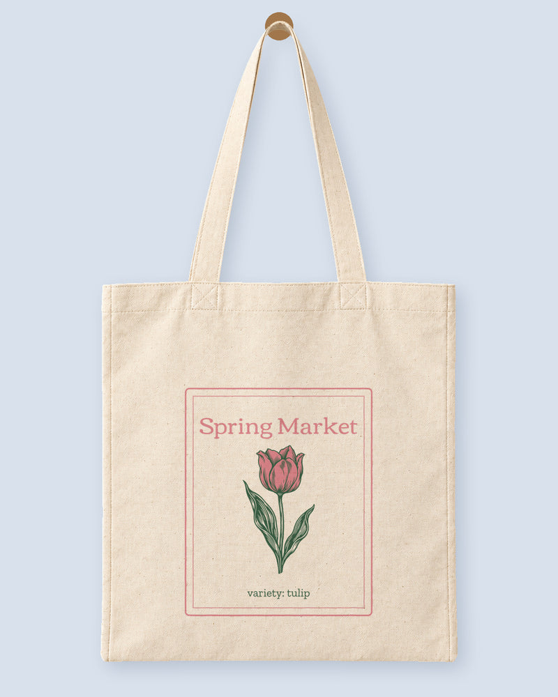 Natural canvas tote printed with “Spring Market”, hanging on a wooden peg.