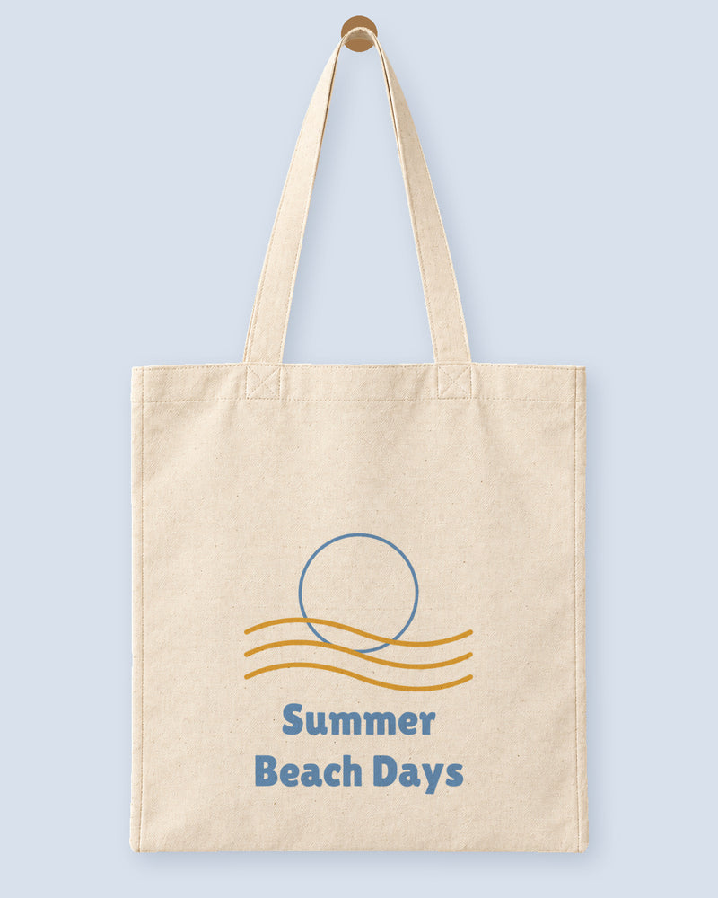 Natural canvas tote printed with “Summer Beach Days”, hanging on a wooden peg.