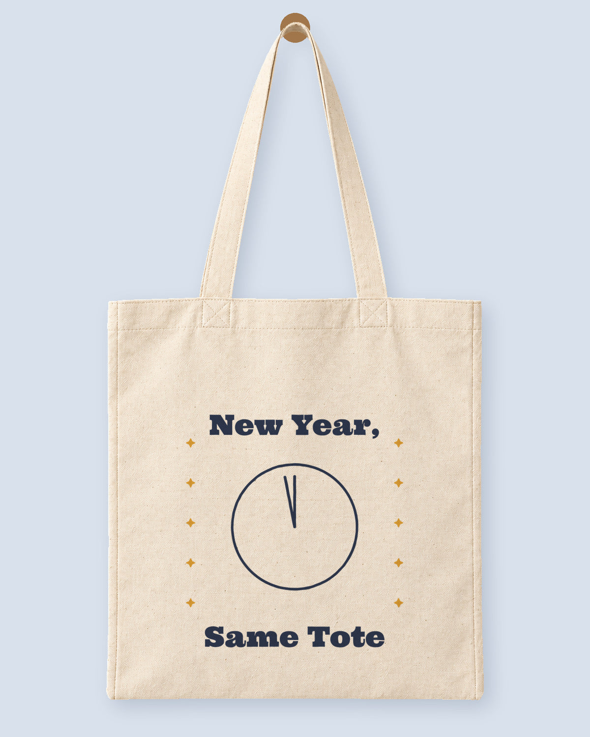 Natural canvas tote printed with “New Year, Same Tote”, hanging on a wooden peg.