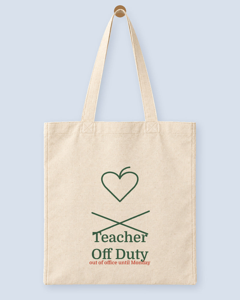 Natural canvas tote printed with “Teacher Off Duty”, hanging on a wooden peg.