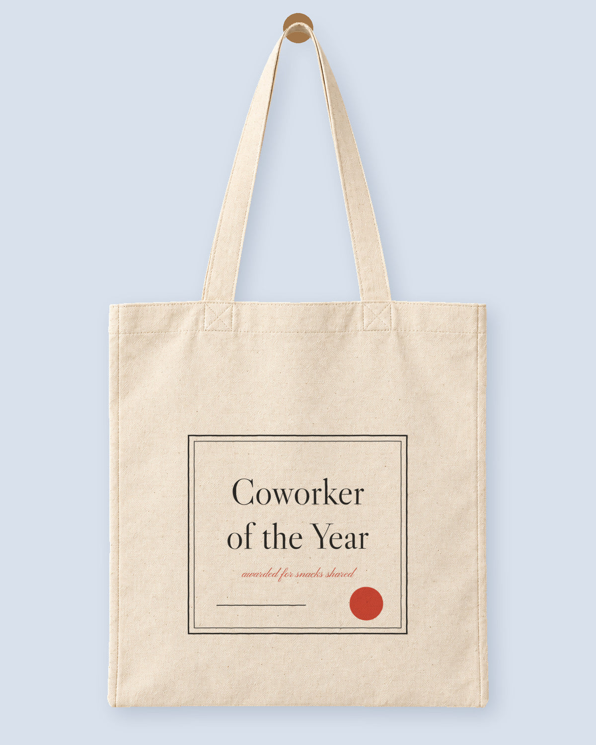Natural canvas tote printed with “Coworker of the Year”, hanging on a wooden peg.