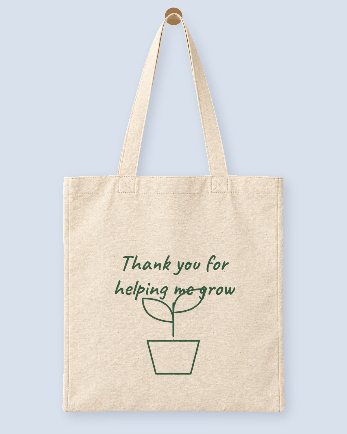 Natural canvas tote printed with “Thank you for helping me grow”, hanging on a wooden peg.