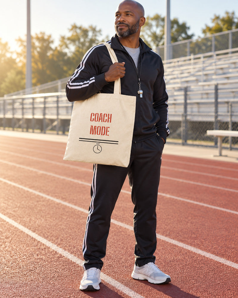 Black man carrying a natural canvas tote printed with “COACH MODE” in red, black. Styled digital image.