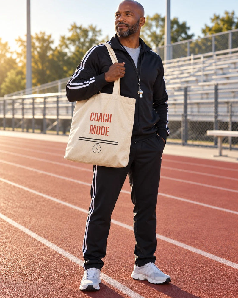 Black man carrying a natural canvas tote printed with “COACH MODE” in red, black. Styled digital image.