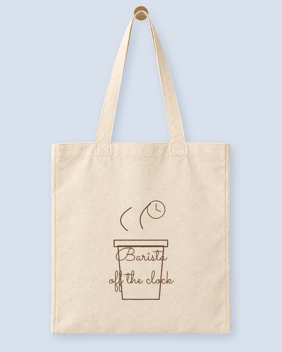 Natural canvas tote printed with “Barista off the clock”, hanging on a wooden peg.