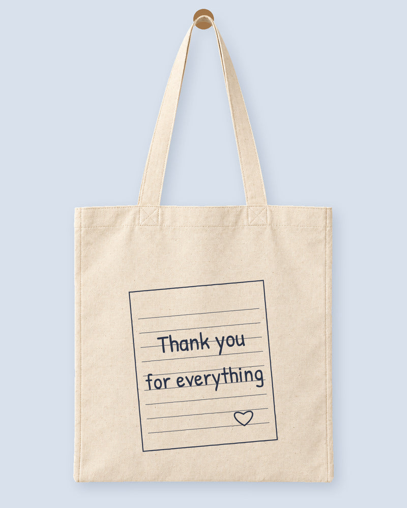 Natural canvas tote printed with “Thank you for everything”, hanging on a wooden peg.