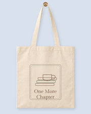 Natural canvas tote printed with “One More Chapter”, hanging on a wooden peg.