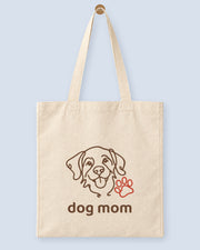 Natural canvas tote printed with “dog mom”, hanging on a wooden peg.