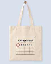 Natural canvas tote printed with “Sunday Errands”, hanging on a wooden peg.