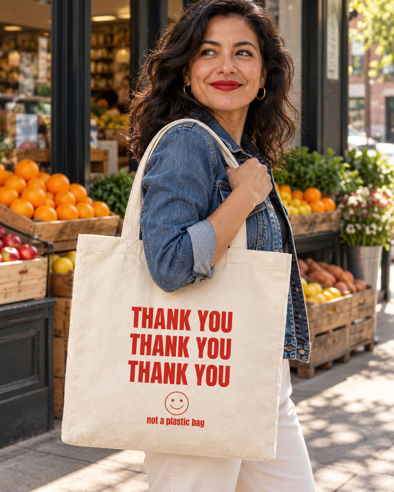 Latina woman carrying a natural canvas tote printed with “THANK YOU” in red. Styled digital image.