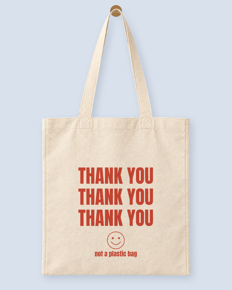 Natural canvas tote printed with “THANK YOU”, hanging on a wooden peg.